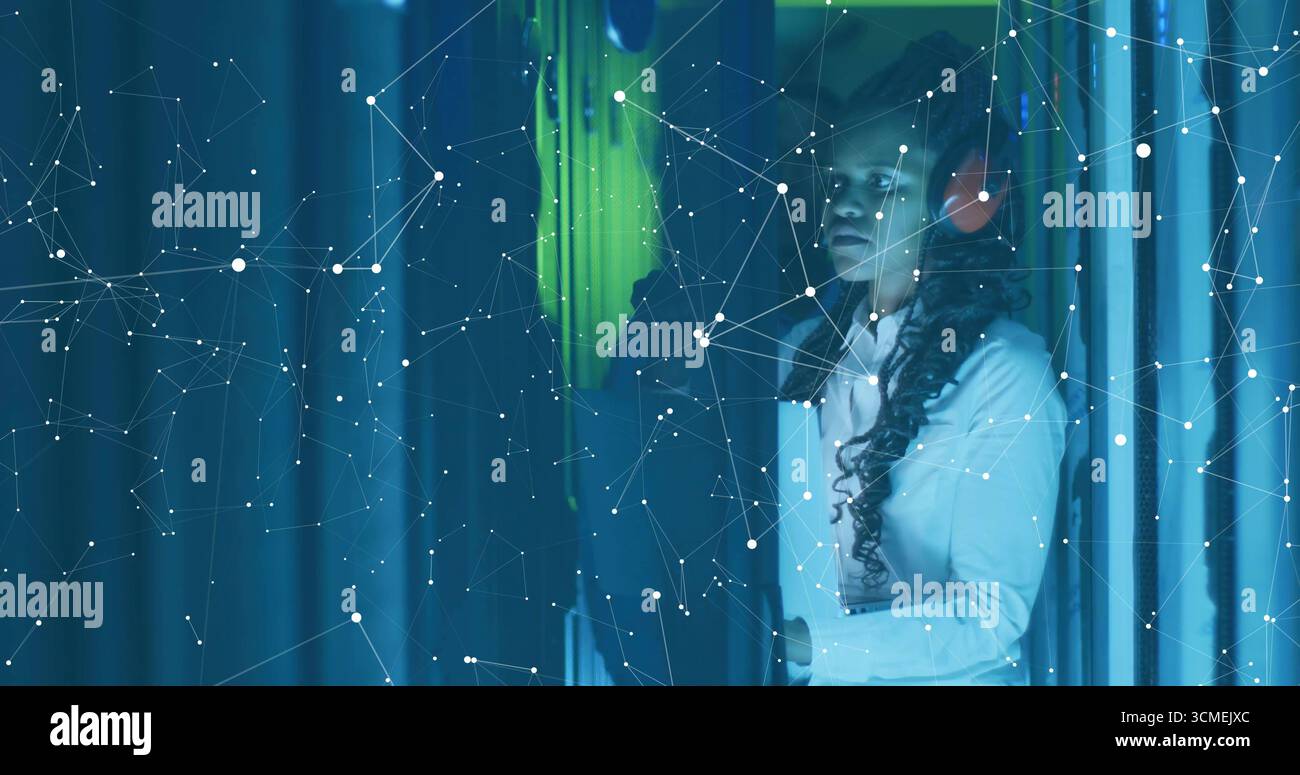 Two IT techs inspecting server racks in data center with headphones, network overlay, copy space Stock Photo