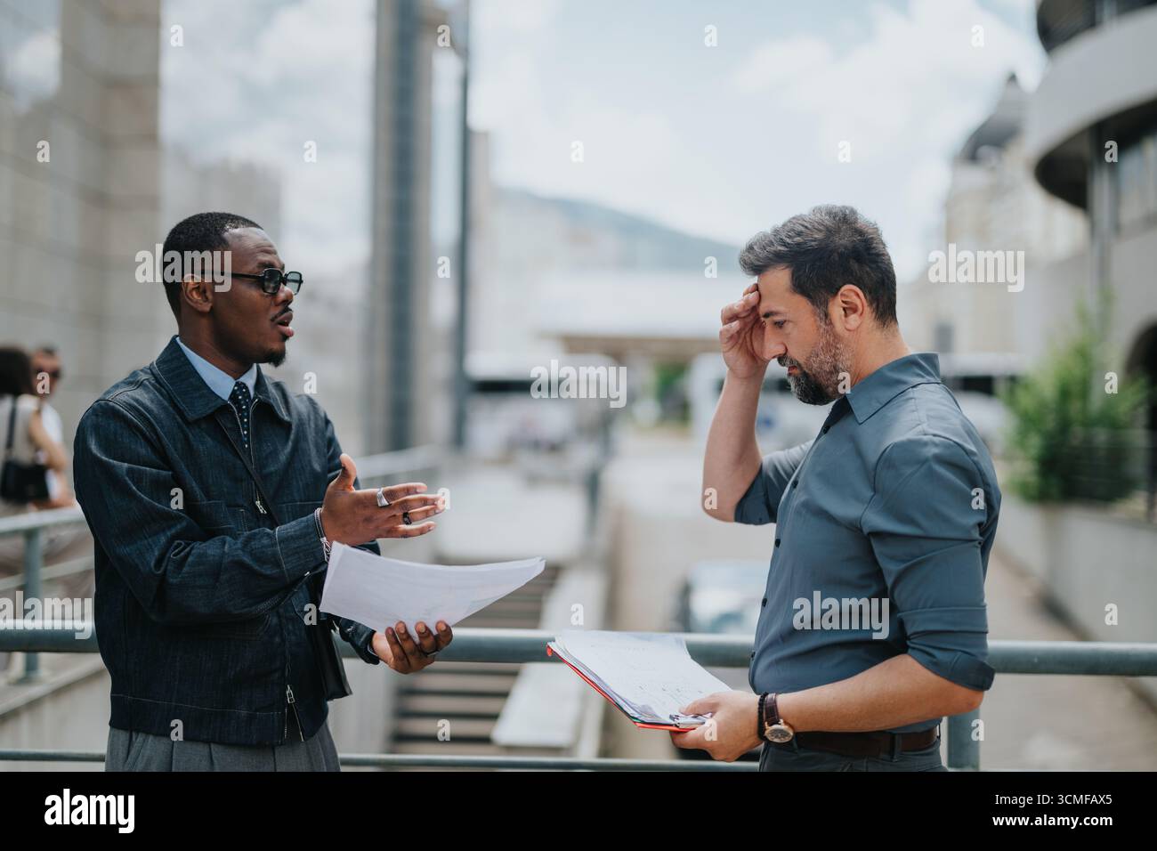Two businessmen discussing a project while reviewing documents outdoors Stock Photo