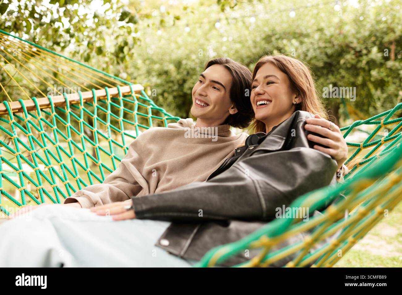A loving couple relaxes in a hammock, sharing smiles and laughter in a serene outdoor setting. Stock Photo
