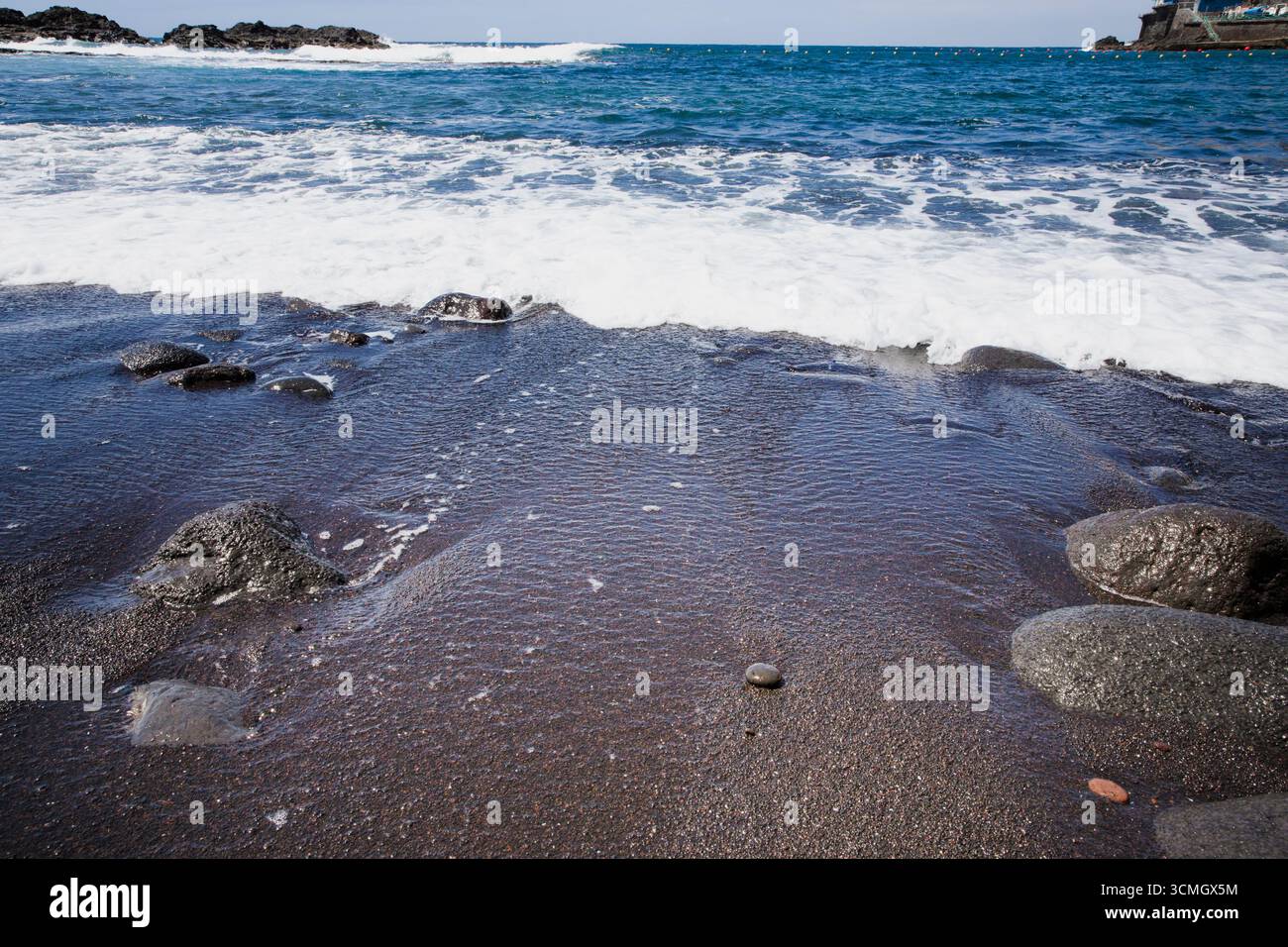 Ocean waves washing black volcanic sand beach with rocks in Tenerife ...