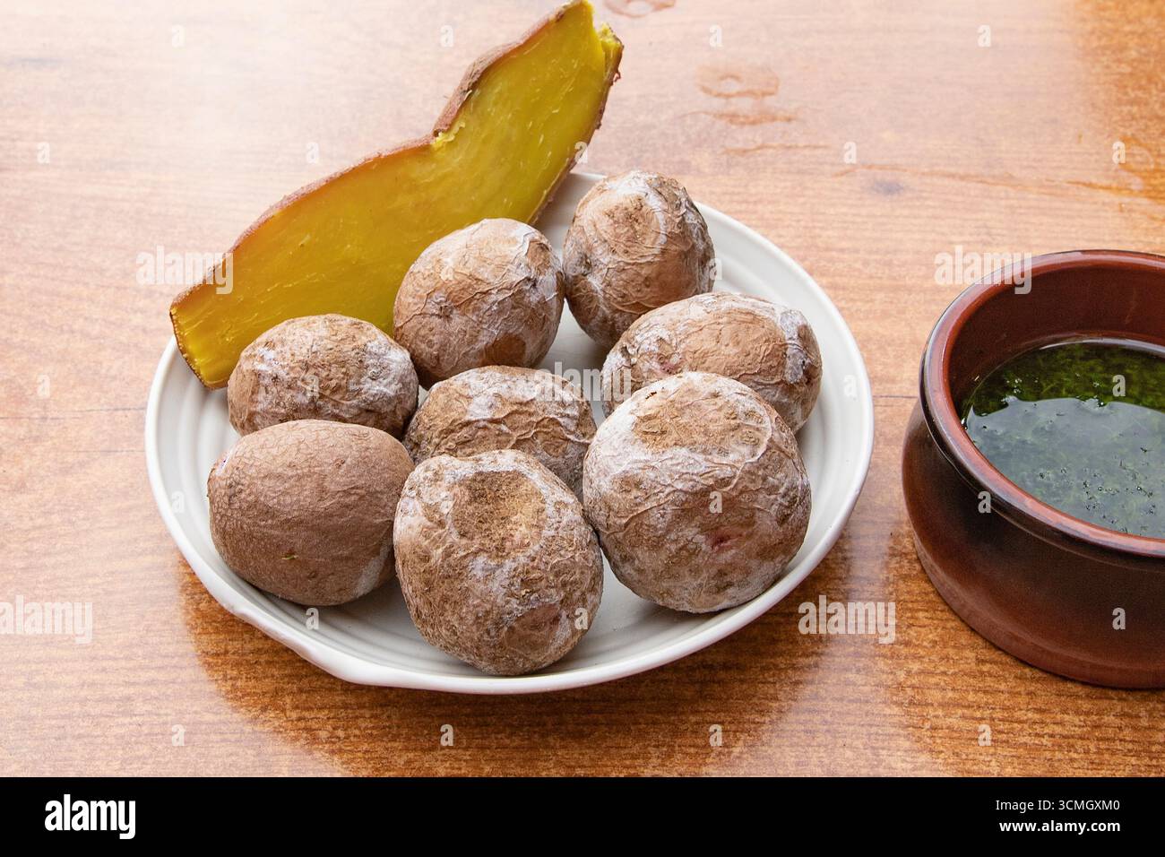 Traditional Canarian wrinkled potatoes papas arrugadas served with green mojo sauce and pumpkin slice. Typical Canary Islands cuisine concept, Spanish Stock Photo