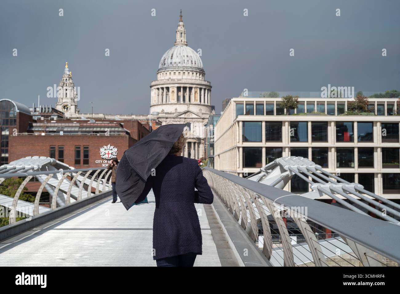 A city worker holding an umbrella on a windy afternoon across the Millennium Bridge towards the City of London, England, UK Stock Photo