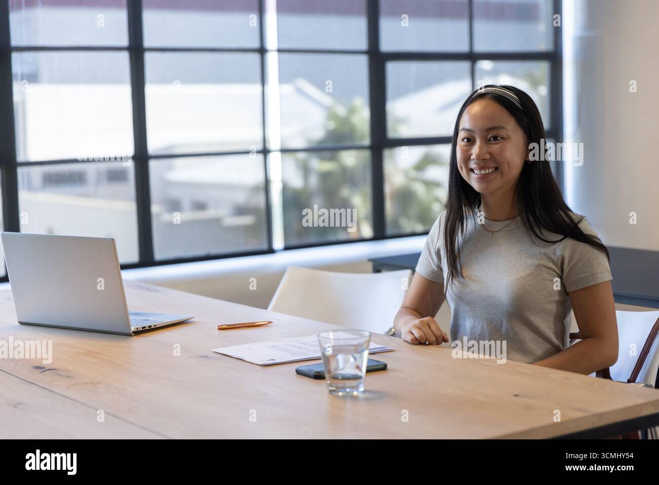 Chinese woman sitting at meeting table typing on laptop checking papers and smartphone, copy space. Professional, collaboration, modernity, productivi Stock Photo