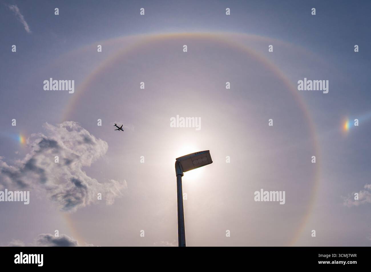 Spectacular halo around the sun with airplane and clouds. 22 degree circle, upper tangent arc, parhelia and part of parhelic circle visible. Stock Photo