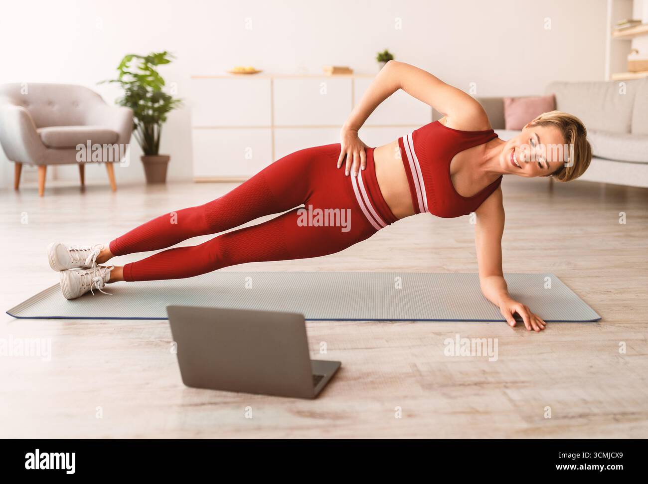 Smiling woman doing side plank on mat with pc Stock Photo