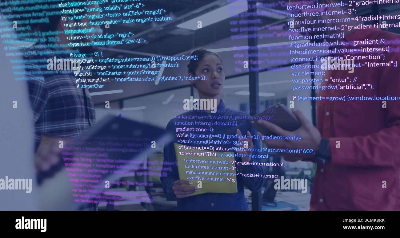 Holding tablet denim-jacketed engineer listening in open office, with code overlay and monitors Stock Photo