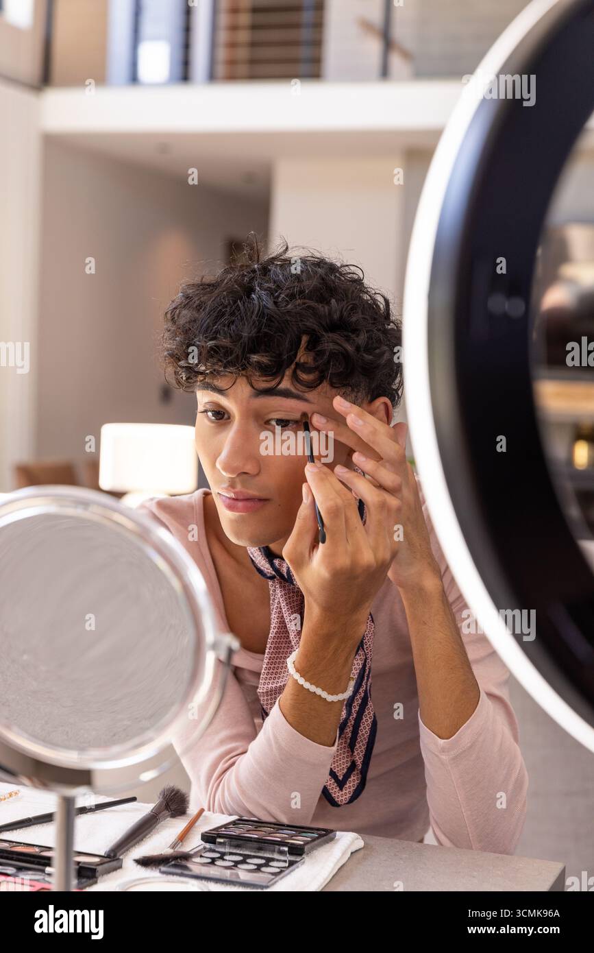 Man applying eyeliner while using mirror under ring light with palettes in living area Stock Photo