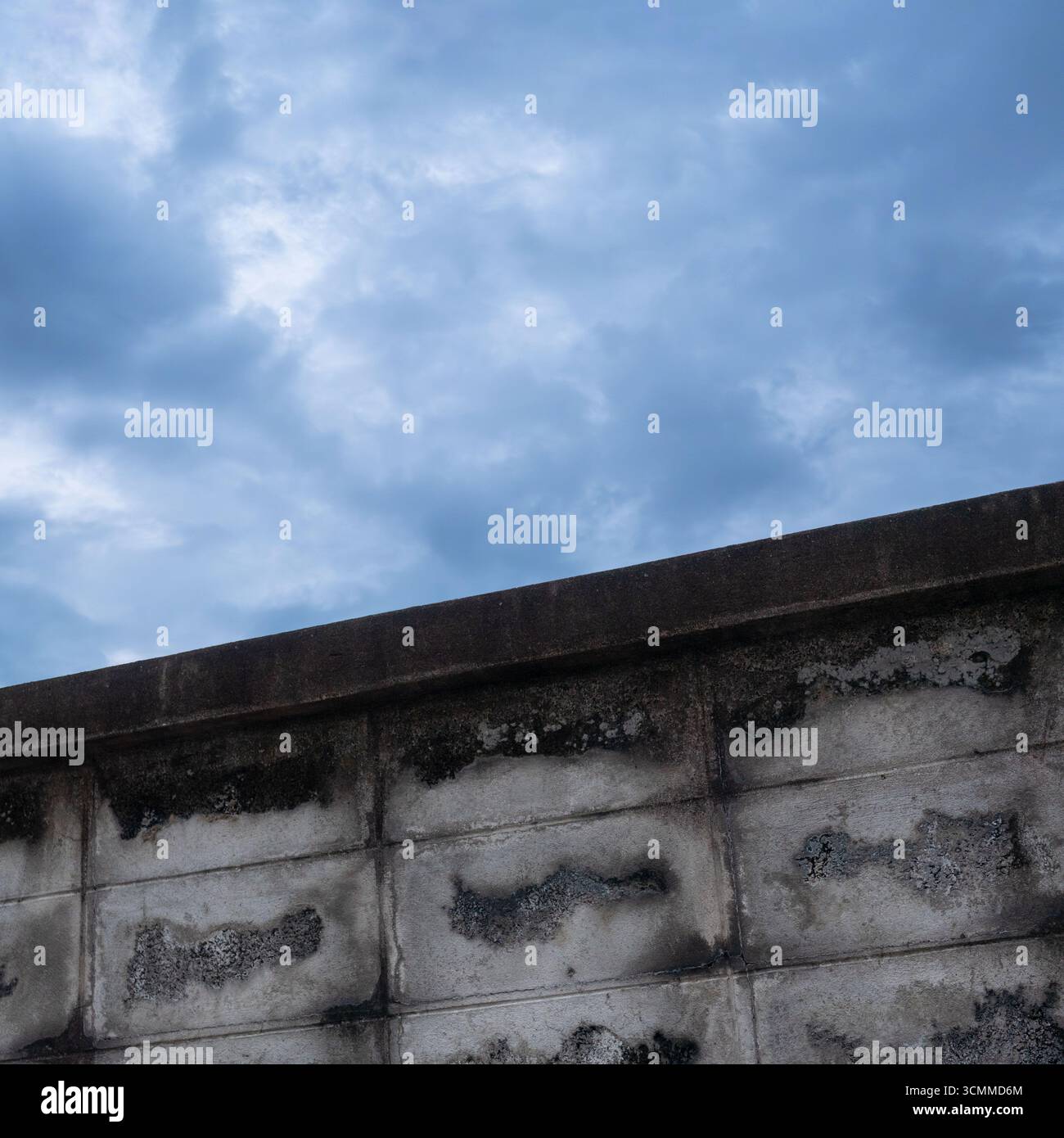 Old grey concrete blocks wall with cloudy blue sky Stock Photo