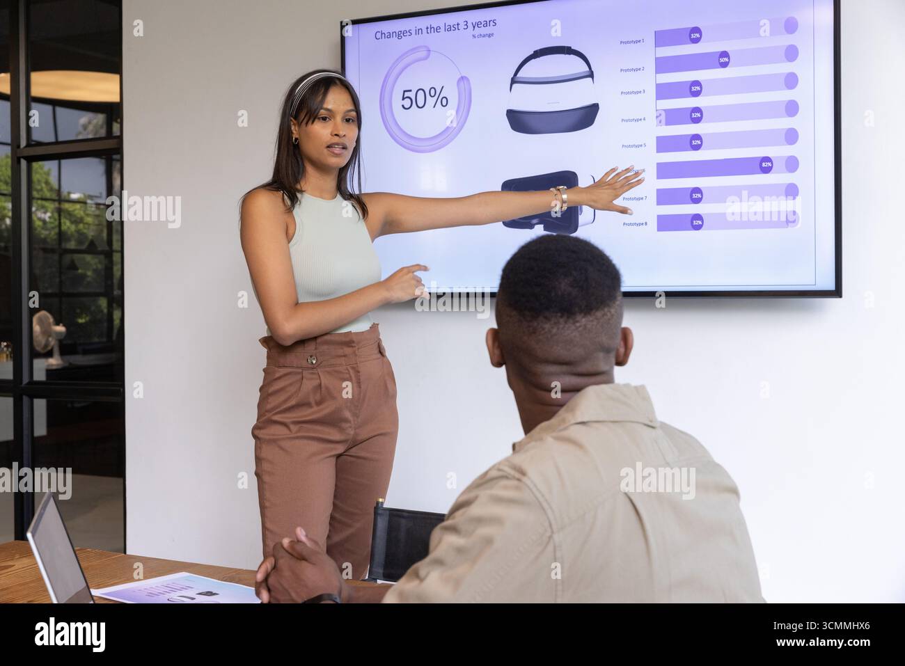 Diverse colleagues presenting charts on display, discussing data via laptop at boardroom table Stock Photo