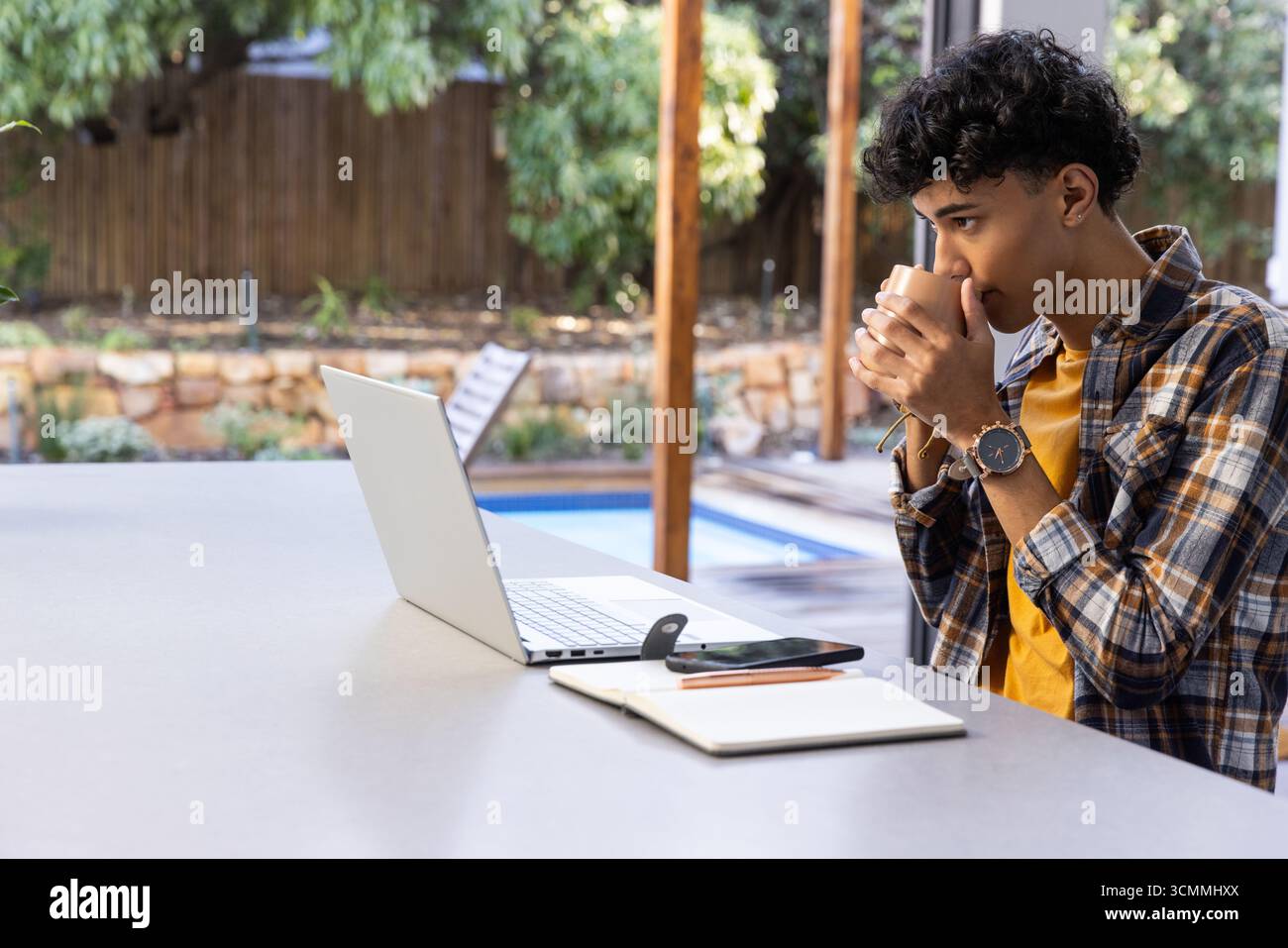 African american man sitting at patio table with coffee mug and using laptop, copy space Stock Photo