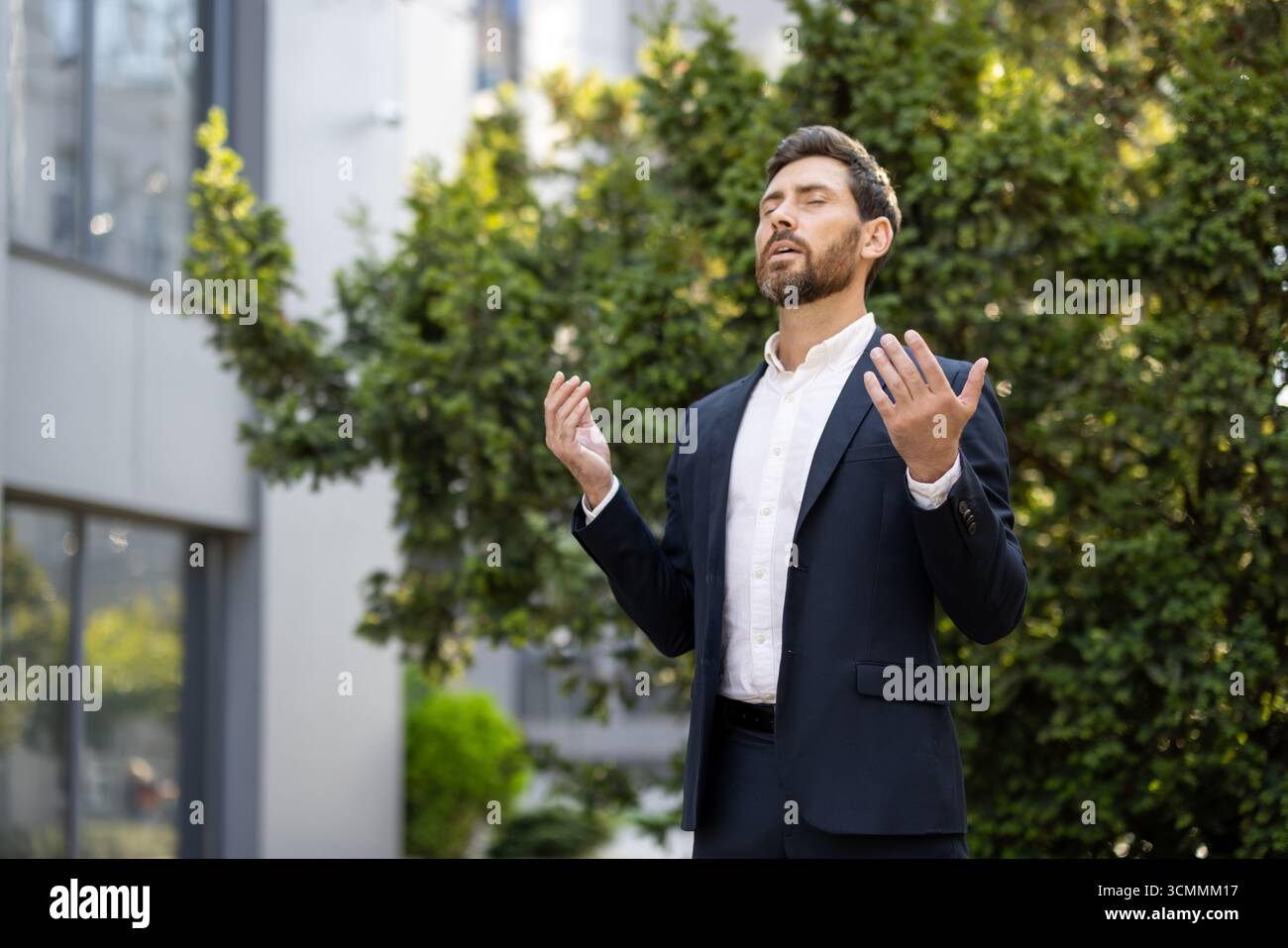 Businessman in suit practicing mindfulness meditation outdoors, relieving stress by practicing breathing exercises in a green urban environment, promo Stock Photo