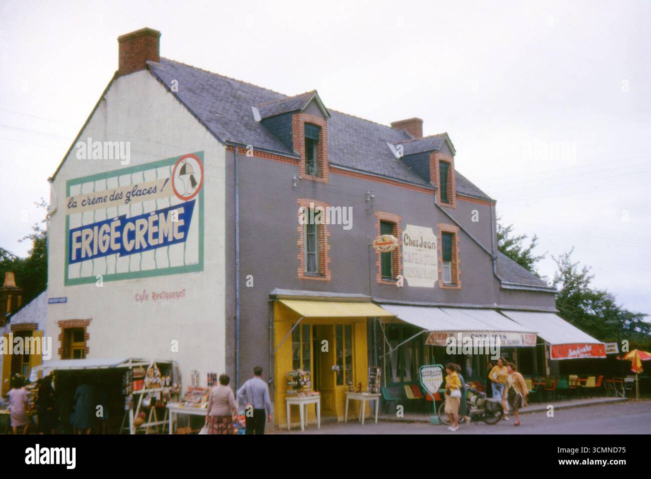 Café-hôtel Chez Jean with Frigécrème mural in Pontchâteau, Loire-Atlantique, France, 1963, featuring street life and shopfronts. Stock Photo