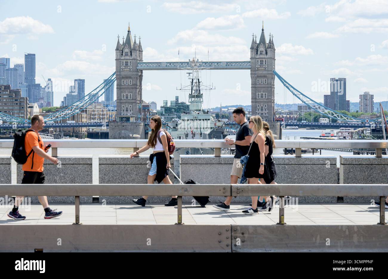 London, UK. People crossing London Bridge with Tower Bridge and HMS Belfast behind them Stock Photo