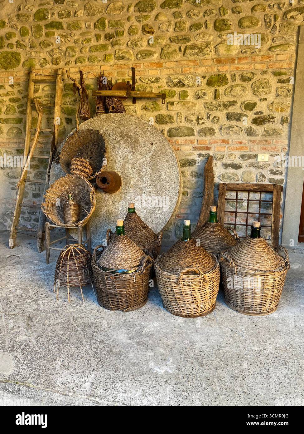 An original millstone wheel with special carved grooves designed for use in grinding chestnuts into flour with a group of squat bottles each enclosed - Smartphone Captured Stock Image