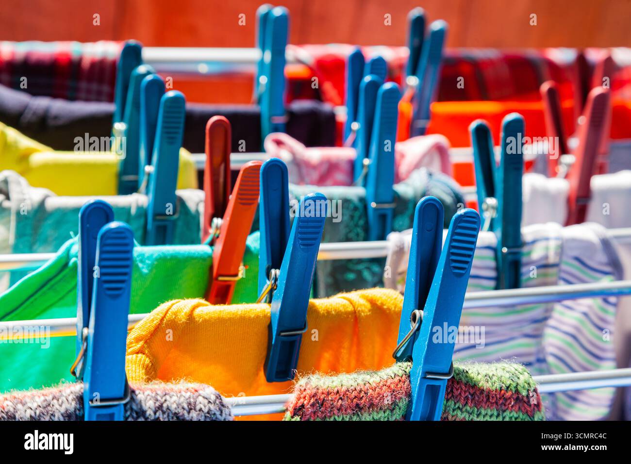 Multi-colored clothes hang attached to clothespins and dry after washing, close-up. Stock Photo
