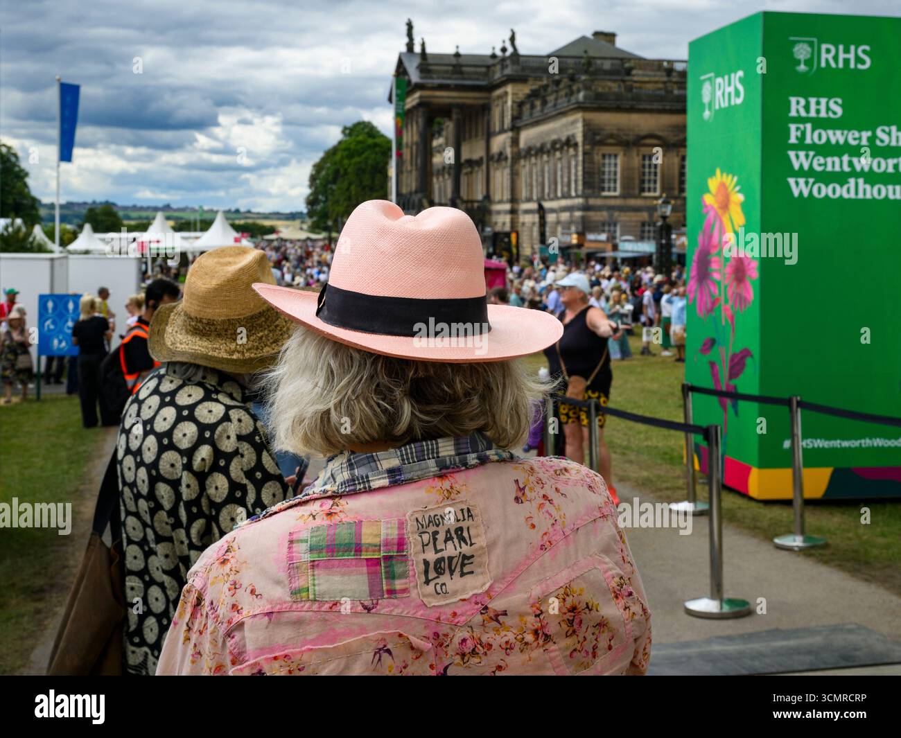 People (close-up) arrive & wait in line, staff scan tickets, mansion ...