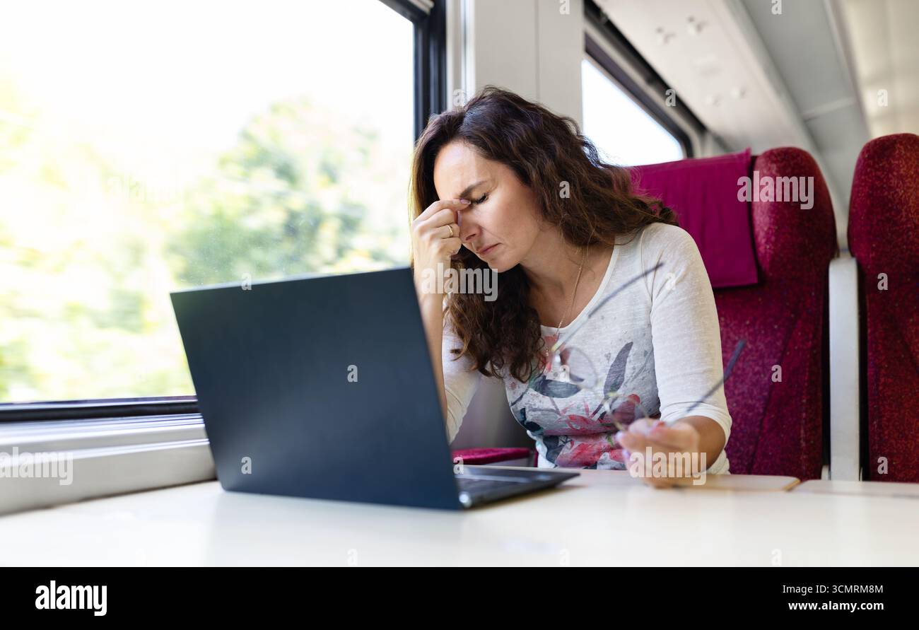 Young Caucasian woman on train feeling tired while using laptop Stock Photo