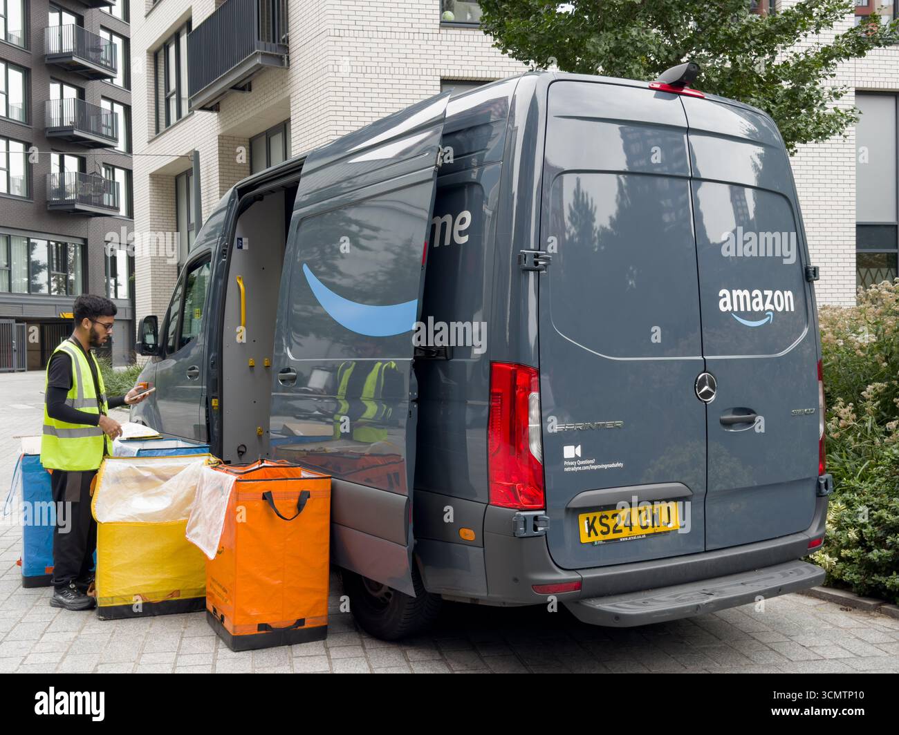 An UK Amazon delivery driver in a high-viz jacket checks three colour ...