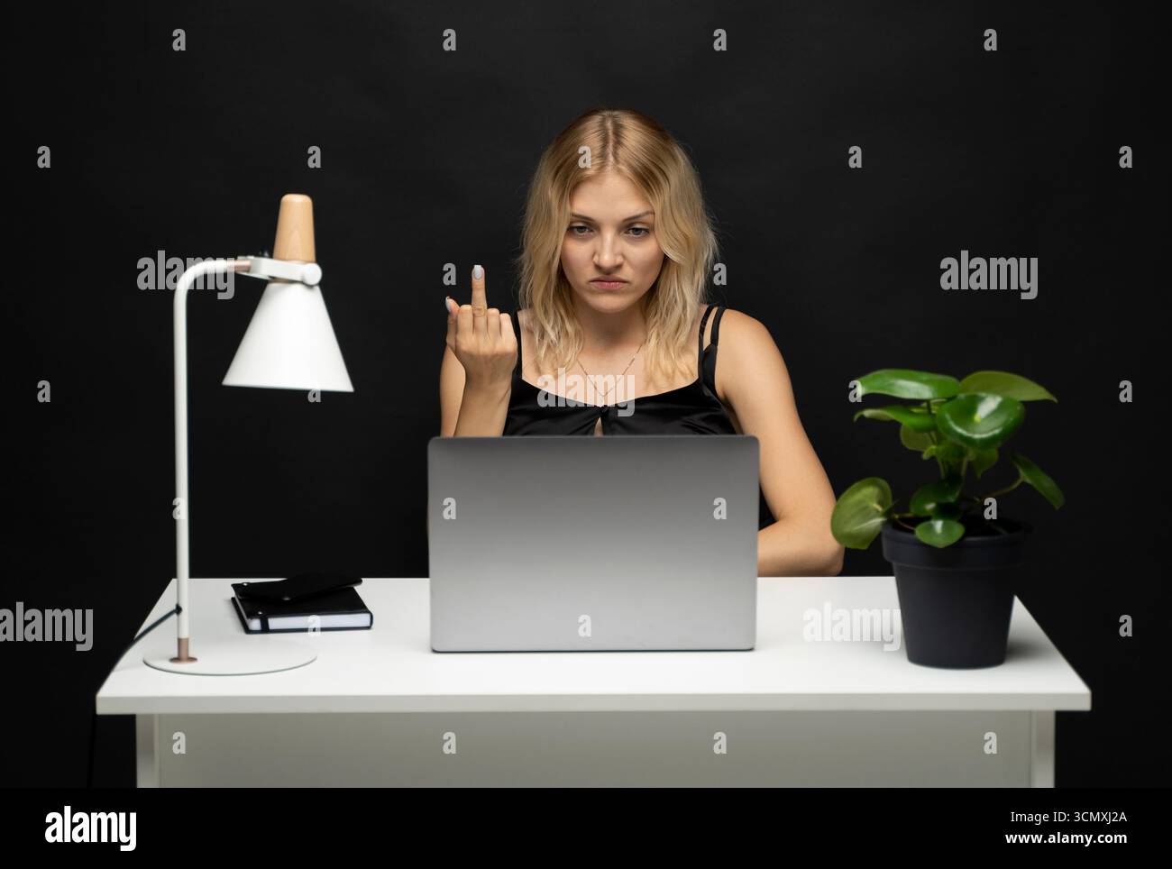 Angry young woman at desk showing rude gesture while working on laptop ...
