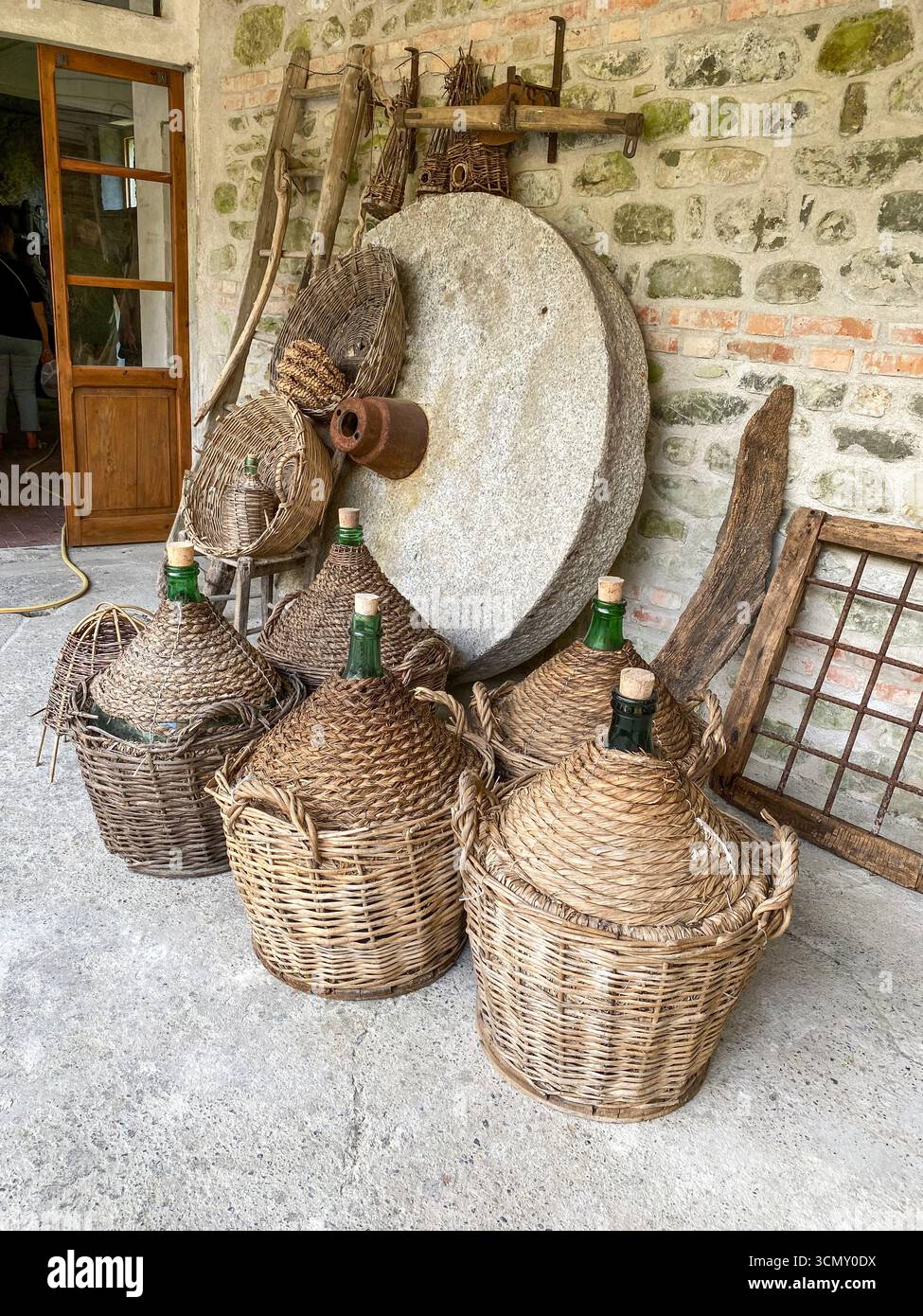 An original millstone wheel with special carved grooves designed for use in grinding chestnuts into flour with a group of squat bottles each enclosed - Smartphone Captured Stock Image