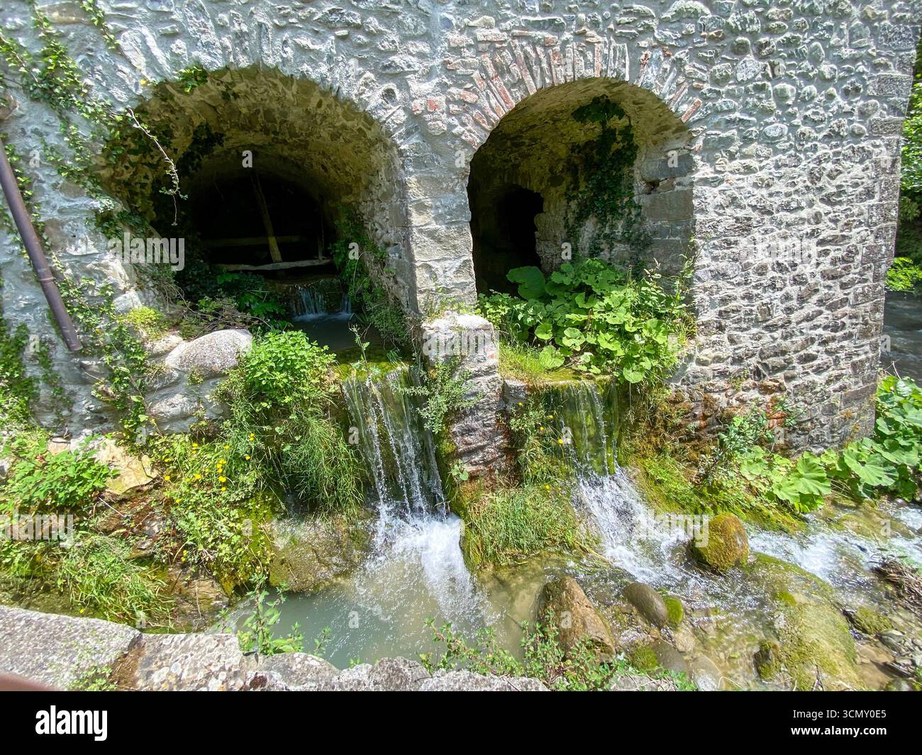 Water pouring from the three tunnels of an old non-functioning watermill  into the Fiume Rosaro (Rosaro River) in the province of Massa-Carrara C a mo - Smartphone Captured Stock Image