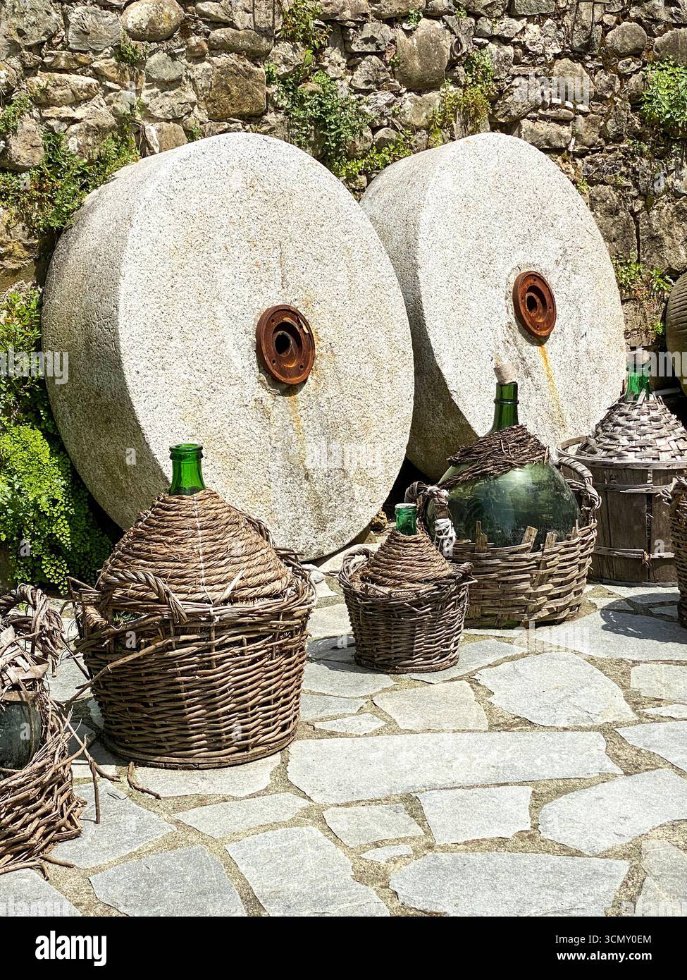 A pair of original millstone wheels with special carved grooves designed for use in grinding chestnuts into flour with a group of squat bottles each e - Smartphone Captured Stock Image