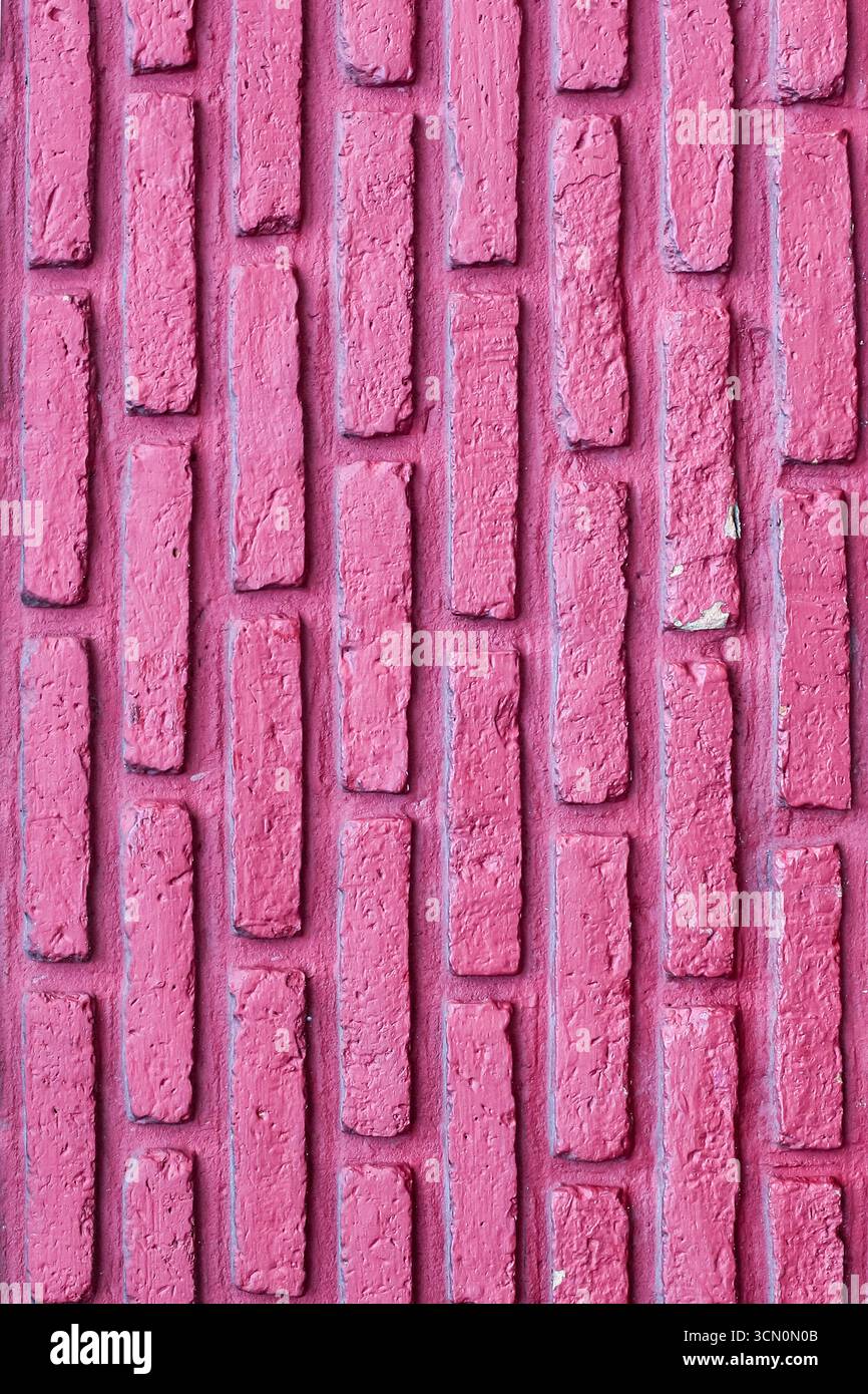 Vertical pink red brick wall with uniform pattern, rough texture, and visible mortar lines, creating a rustic abstract design background. Stock Photo
