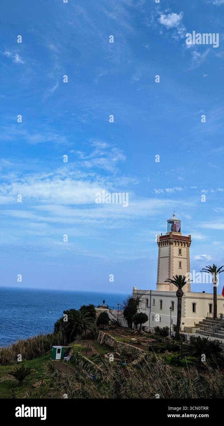 Iconic Phare du Cap spartel lighthouse, overlooking the meeting of the Mediterranean and atlantic amid plam trees and blue sky - Smartphone Captured Stock Image
