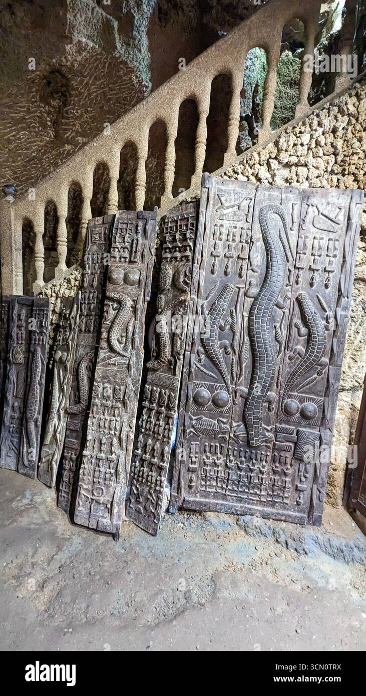 Collection of wooden panels featuring crocodile/snake motifs, displayed inside the historic Caves of Hercules, Tangier, Morocco. - Smartphone Captured Stock Image