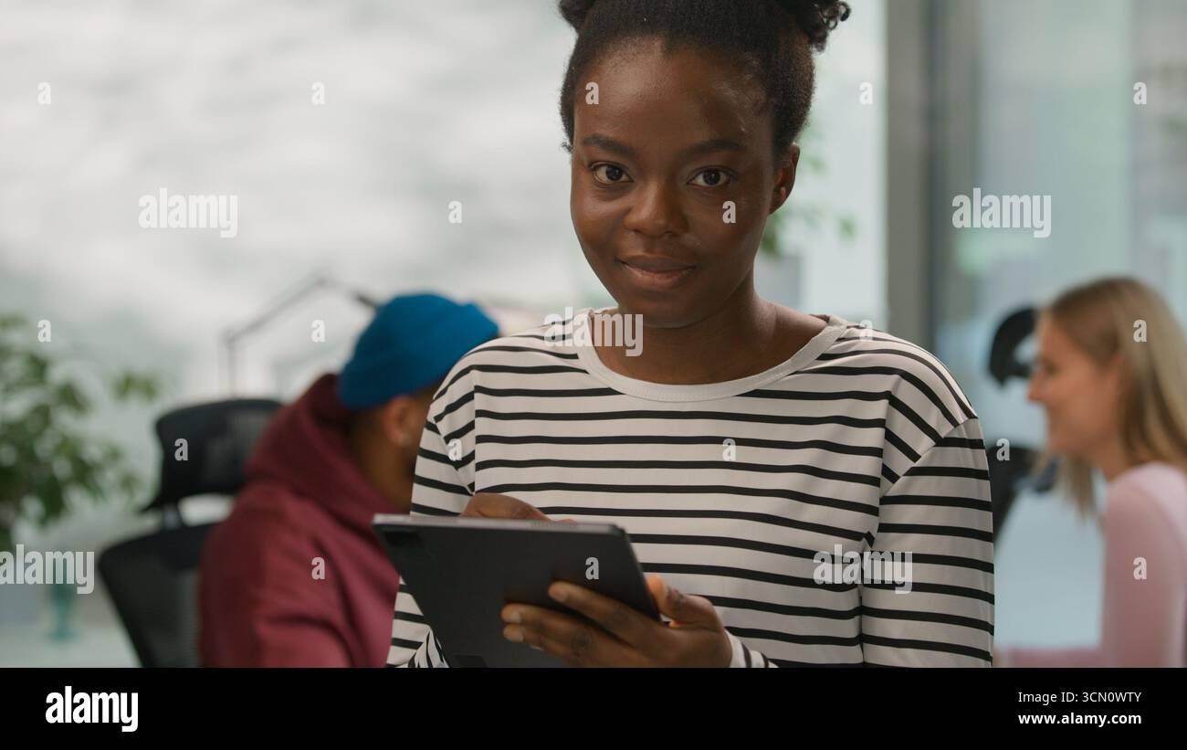 Portrait African American casual businesswoman typing digital tablet online app looking at camera smiling informal business woman female girl in Stock Photo