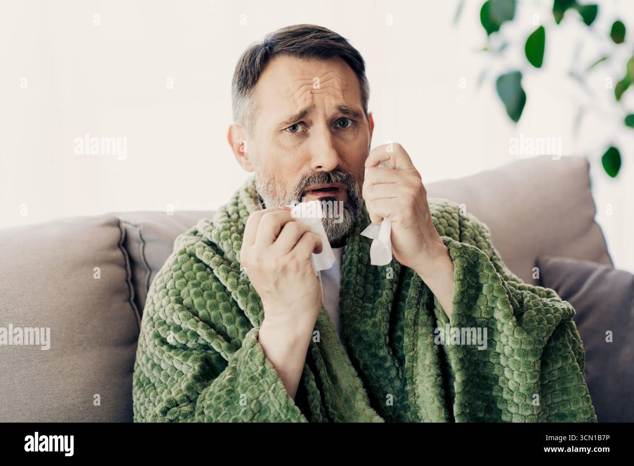 Unwell Man Middle aged man relaxing at home while feeling unwell and wrapped in a ...