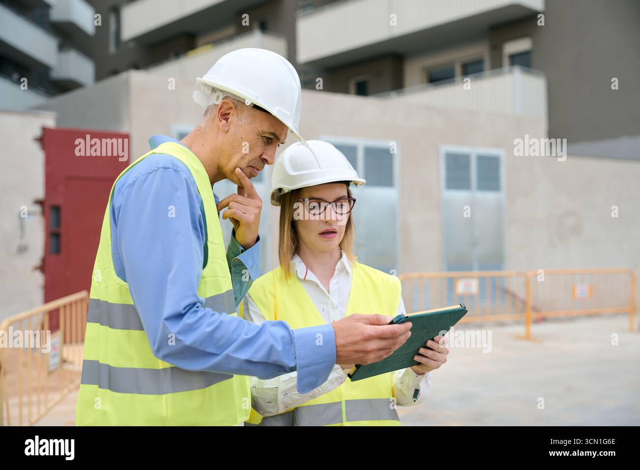 Engineers reviewing construction plans on tablet at building site Stock Photo