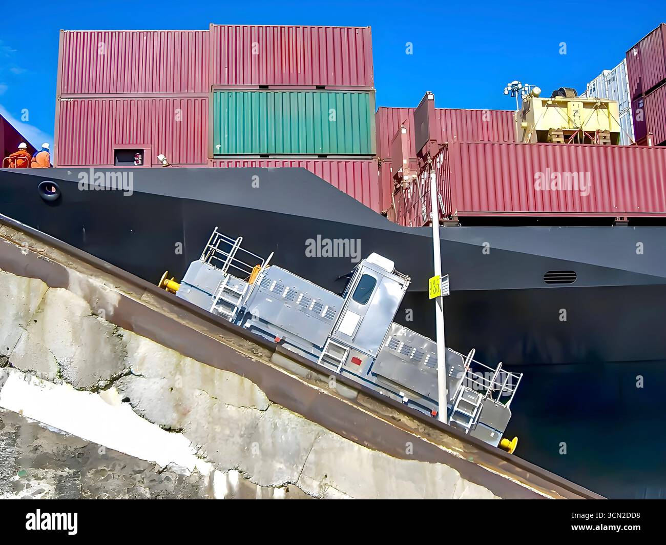 A Panama Canal 'mule' locomotive on a sloped track alongside a large container ship during transit through the canal's lock system. Stock Photo