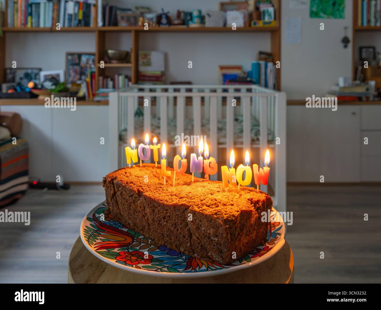 “Not long now” lettering on a cake placed in front of an empty baby crib, symbolizing anticipation and excitement in the last weeks of pregnancy Stock Photo