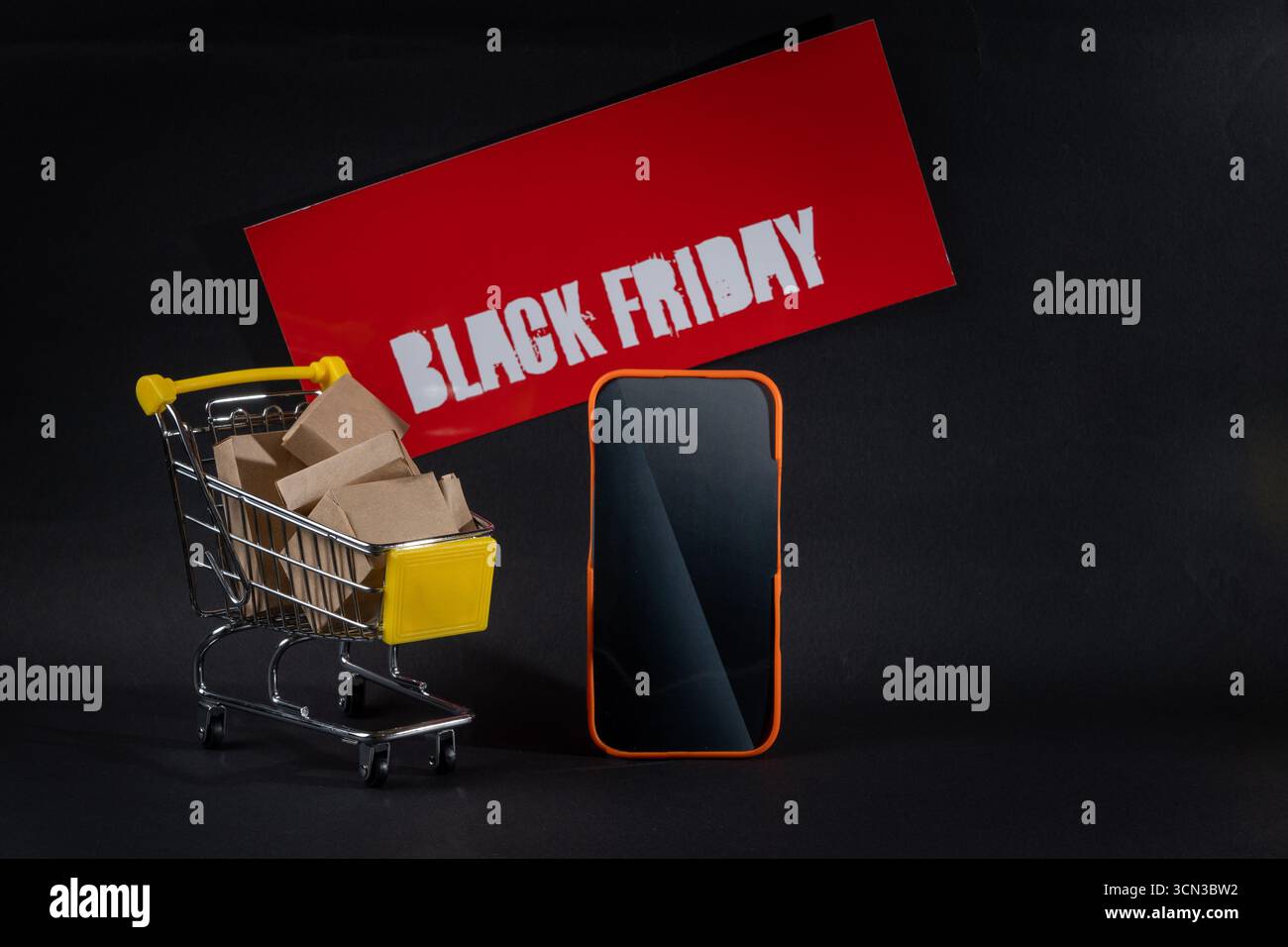 Miniature shopping cart full of cardboard boxes with smartphone and black friday advertising sign on black background representing online shopping and Stock Photo