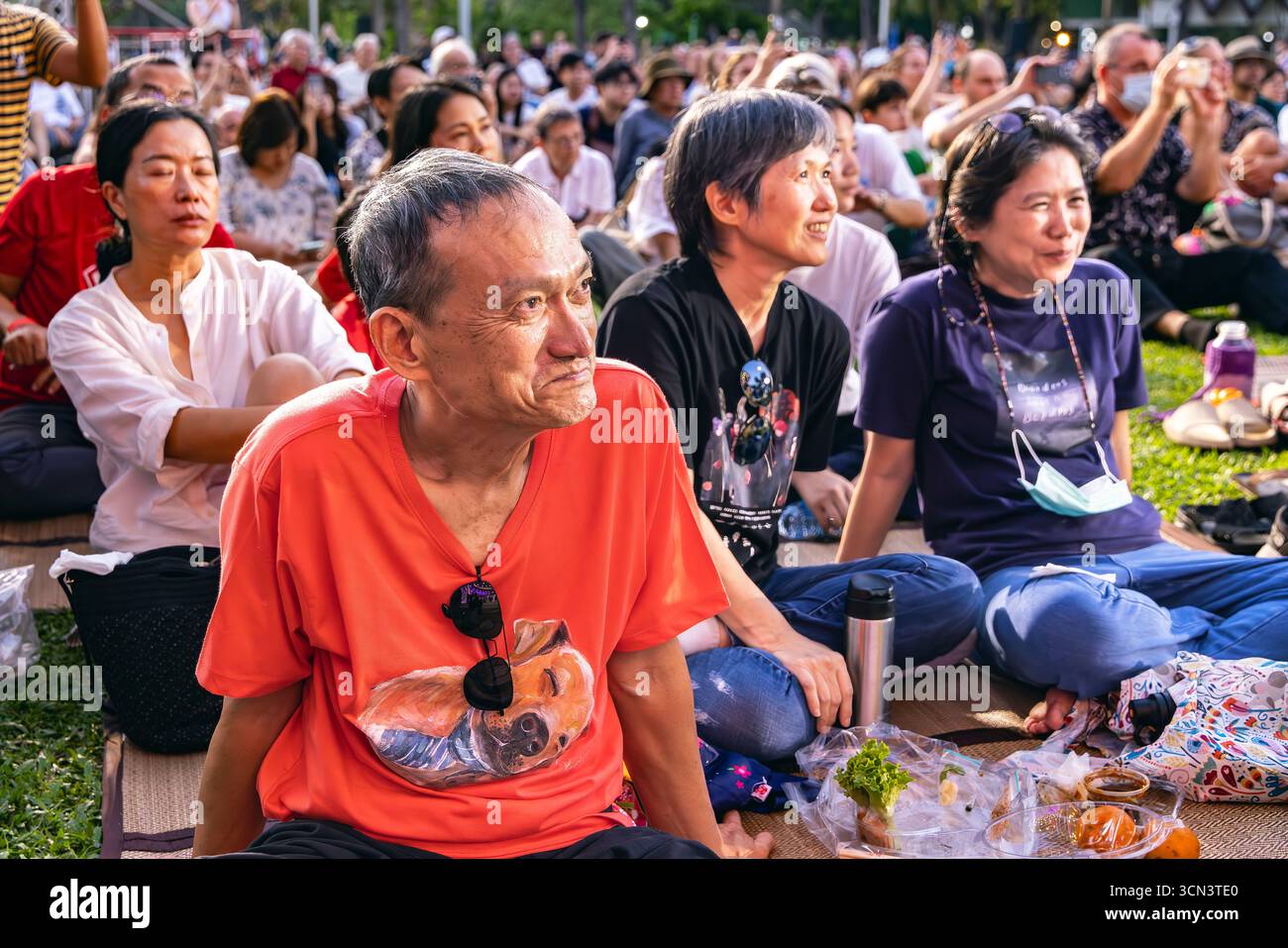 Thai family and tourists sitting on grass watching open air classical music concert in Lumphini Park, Bangkok, Thailand Stock Photo