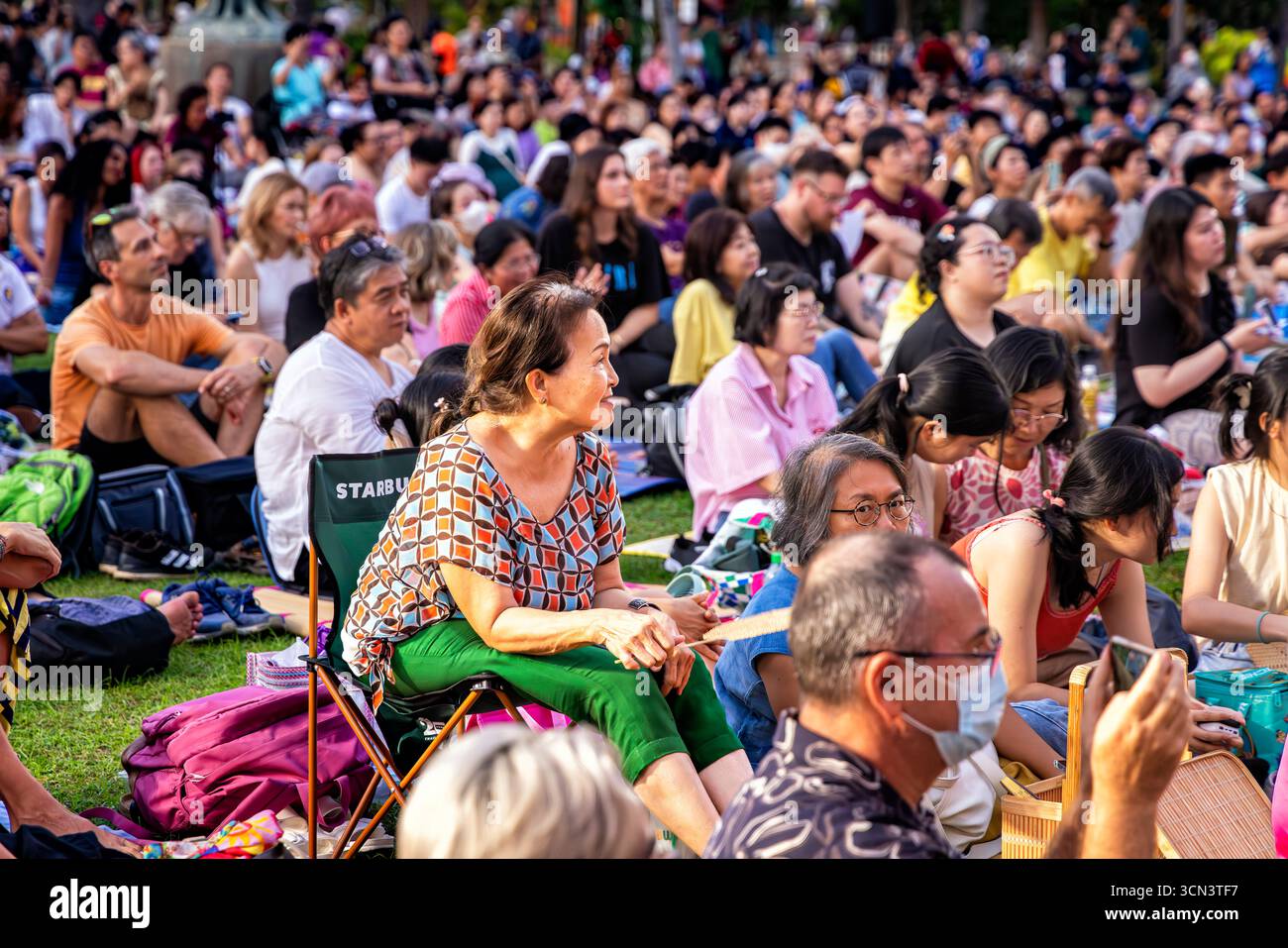 Thai family and tourists sitting on grass watching open air classical music concert in Lumphini Park, Bangkok, Thailand Stock Photo