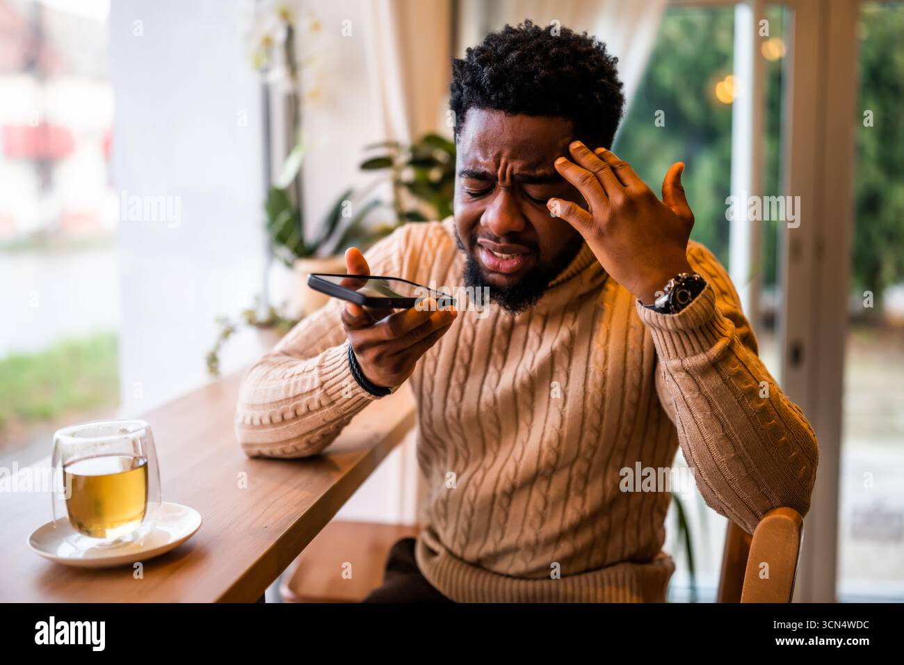 A young black man sits at the bar, casually dressed. He is using smartphone and recording voice message. Stock Photo