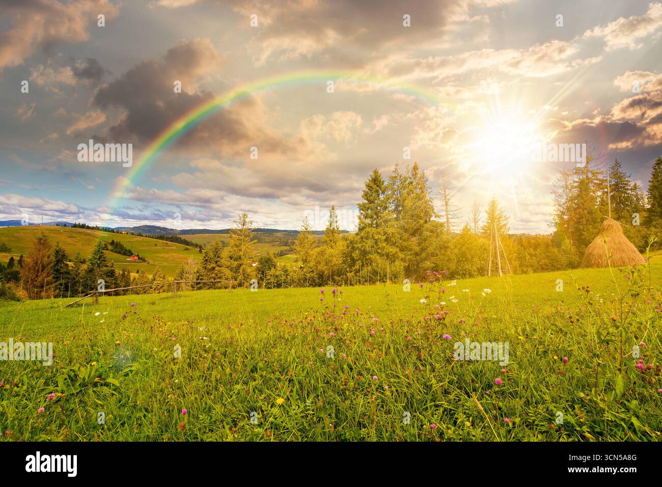 rural area in autumn at sunset. scenic view. countryside scenery with rolling hills under rainbow. mountain landscape in evening light. provincial out Stock Photo
