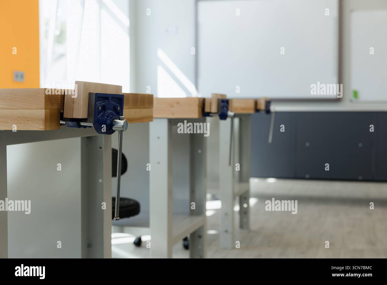 Well-lit workshop features several wooden workbenches, ready for projects in a modern classroom. Stock Photo