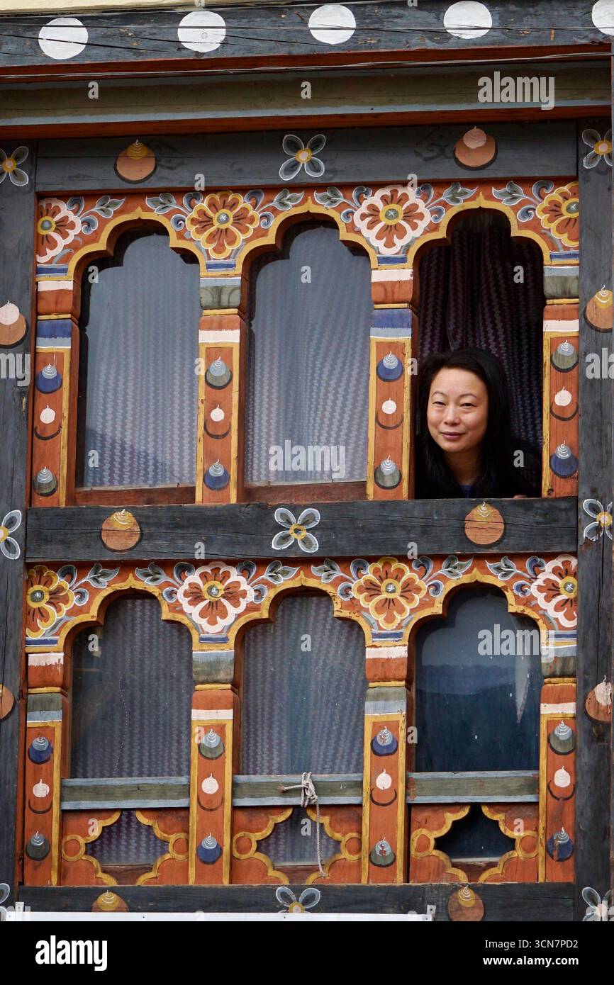 a woman looks out from a traditional window in Bhutan Stock Photo