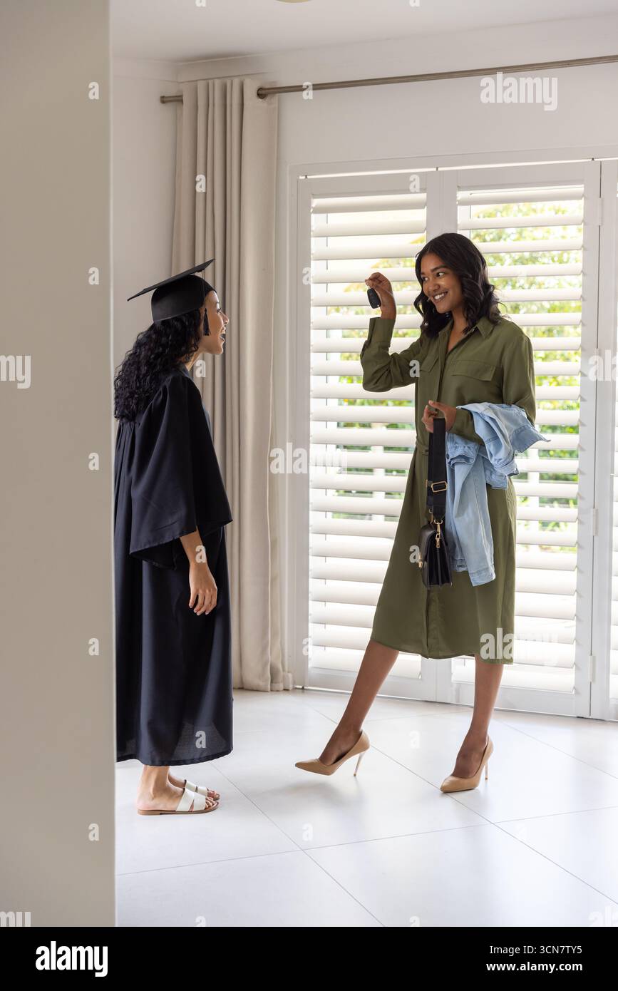 Female graduate in cap and gown receiving keys from mother in foyer, copy space Stock Photo