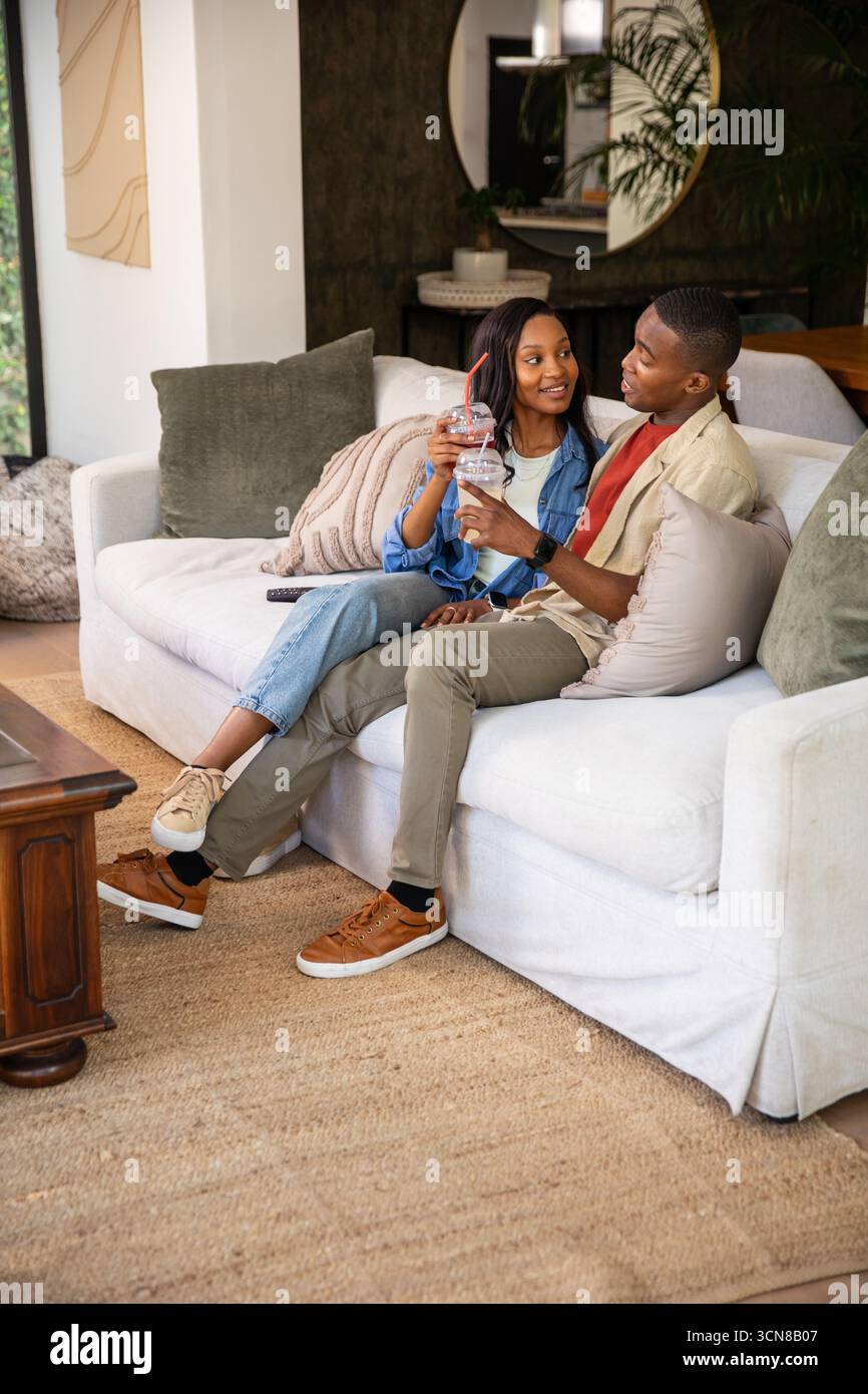 African American couple sitting on sofa in living room sipping iced ...