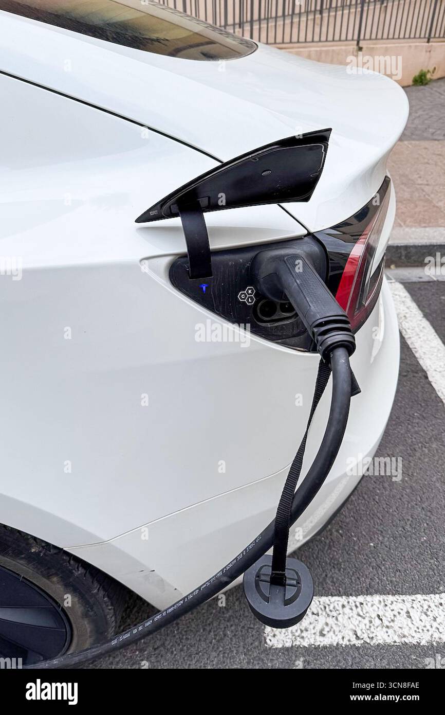 Perpignan, France. 04th Sep, 2025. A white Tesla electric vehicle is plugged in for charging along a street, with the charge port open and the charging connector inserted into the rear left side of the car on Sept. 4, 2025. The scene appears to be in an urban area. (Photo by Samuel Rigelhaupt/Sipa USA) Credit: Sipa USA/Alamy Live News Stock Photo