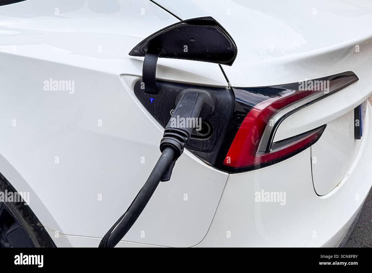 Perpignan, France. 04th Sep, 2025. A white Tesla electric vehicle is plugged in for charging along a street, with the charge port open and the charging connector inserted into the rear left side of the car on Sept. 4, 2025. The scene appears to be in an urban area. (Photo by Samuel Rigelhaupt/Sipa USA) Credit: Sipa USA/Alamy Live News Stock Photo