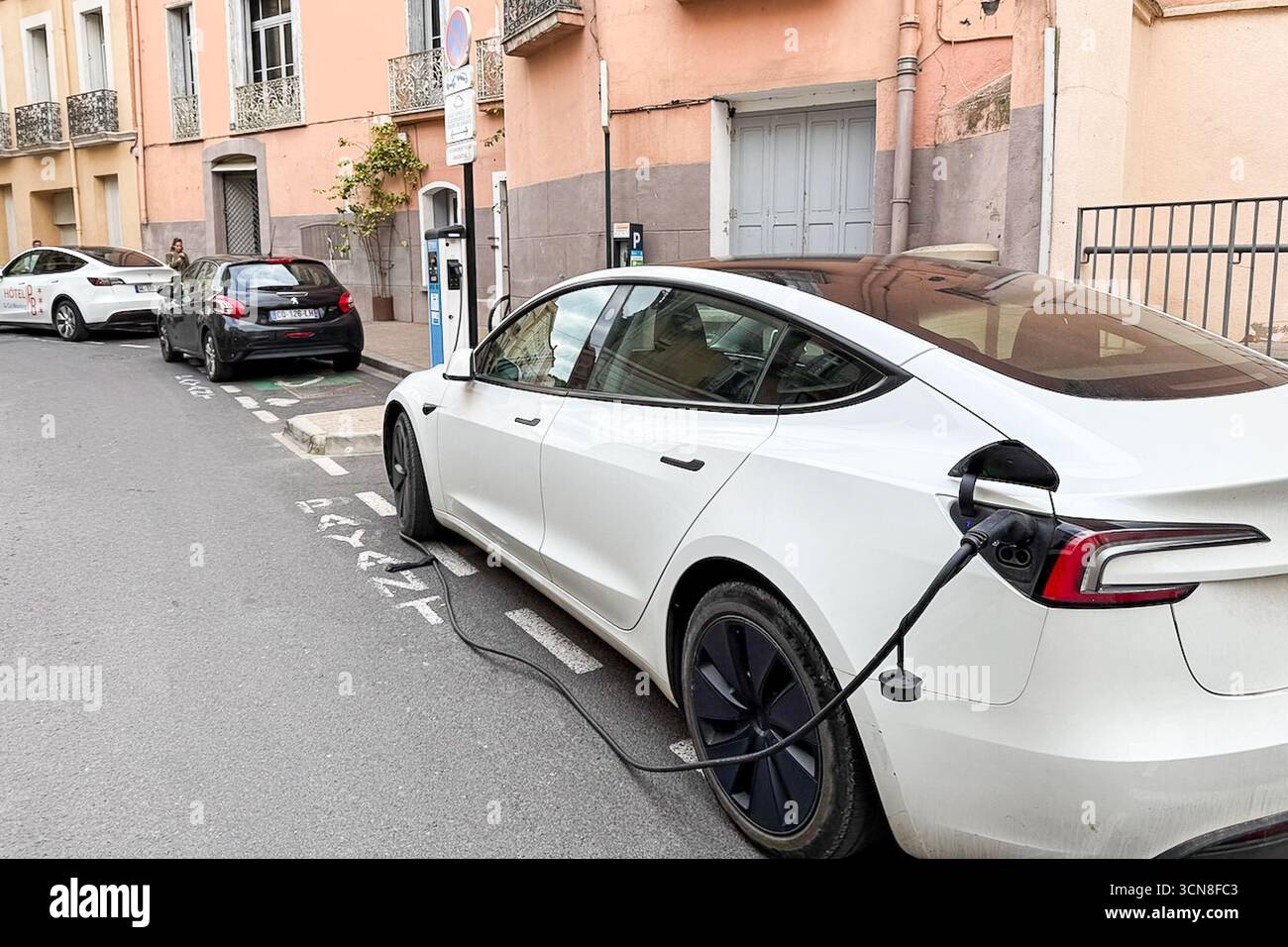 Perpignan, France. 04th Sep, 2025. A white Tesla electric vehicle is plugged in for charging along a street, with the charge port open and the charging connector inserted into the rear left side of the car on Sept. 4, 2025. The scene appears to be in an urban area. (Photo by Samuel Rigelhaupt/Sipa USA) Credit: Sipa USA/Alamy Live News Stock Photo