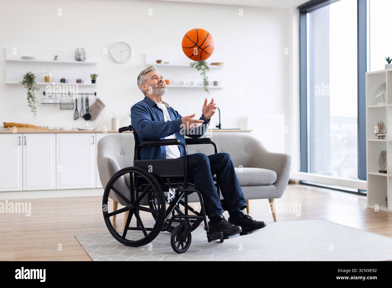 Man in wheelchair practicing basketball in modern living room Stock Photo