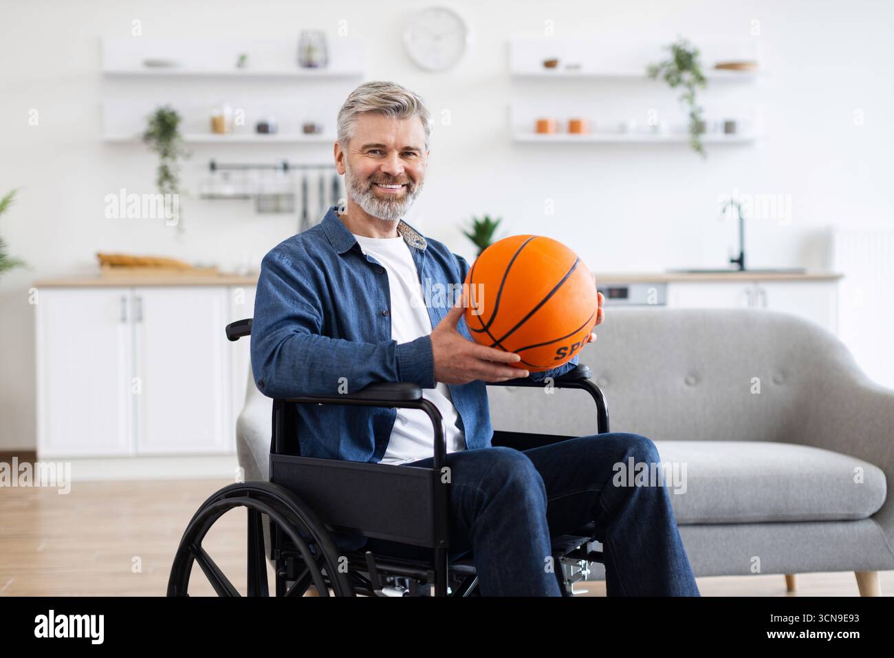 Man practicing basketball while seated in wheelchair in modern home environment Stock Photo