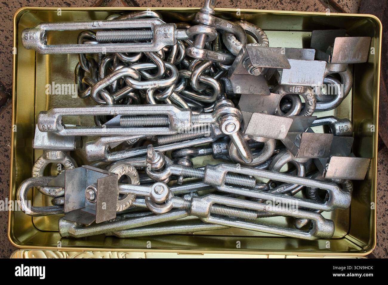A tin of assorted metal objects, including chains and bolts. The tin is open and the objects are scattered around Stock Photo
