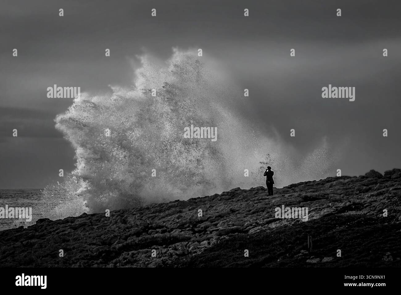 Black and white photo of a giant ocean wave crashing on the rocky shore ...